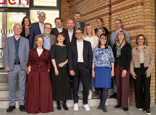 Eine Gruppe von rund 15 Personen steht gemeinsam auf einer Treppe vor einem Gebäude mit Backsteinfassade. Die Teilnehmenden der Kanzlerkonferenz sind in mehreren Reihen angeordnet, lächeln in die Kamera und tragen überwiegend Businesskleidung.